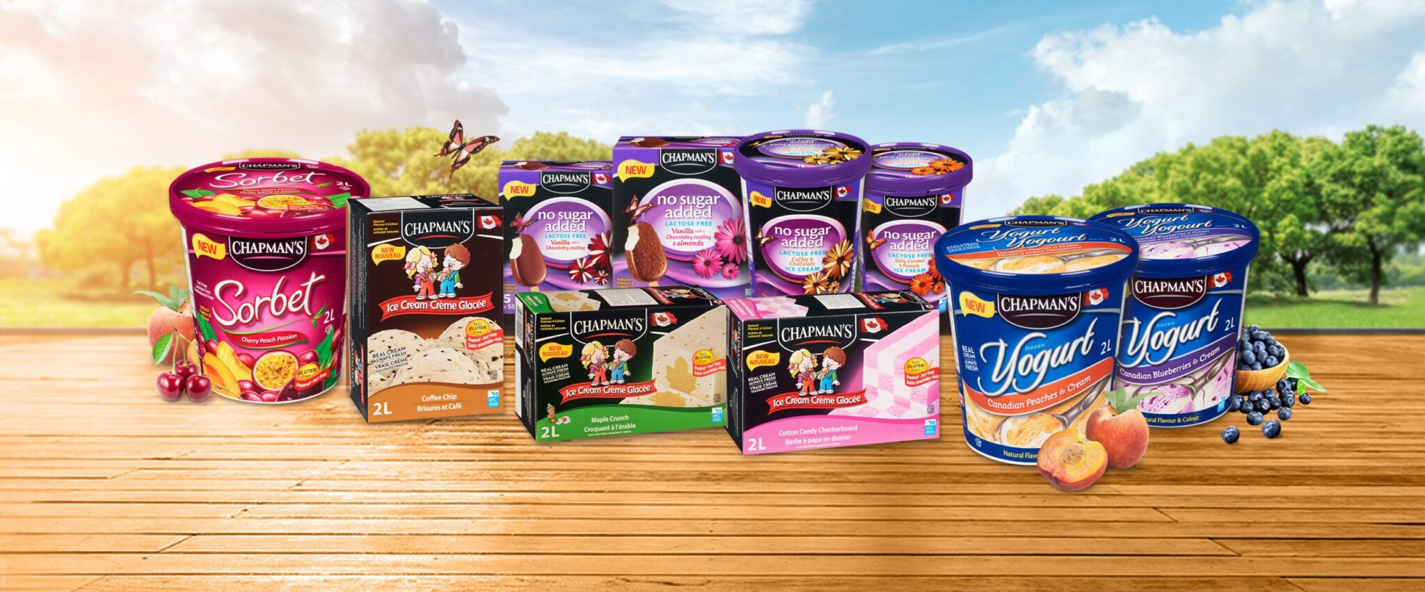 Les 10 nouveaux produits de Chapman’s pour 2022 disposés côte à côte sur une table en bois avec un ciel d’été lumineux et des arbres verts en arrière-plan